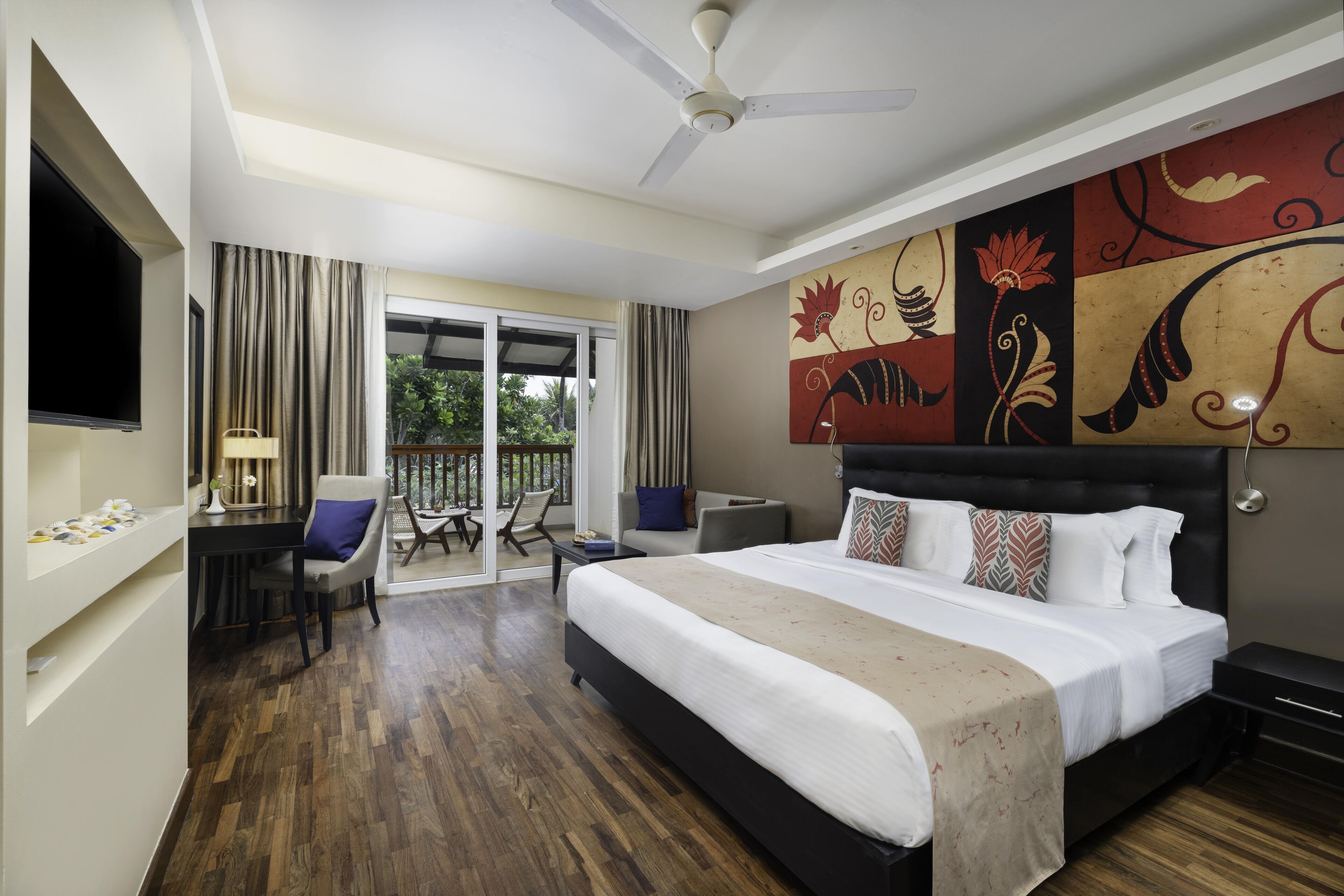 A hotel room with a large bed, a desk, a chair, a TV, and a balcony with curtains.