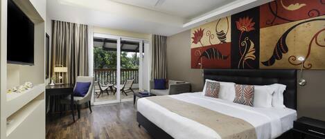 A hotel room with a large bed, a desk, a chair, a TV, and a balcony with curtains.