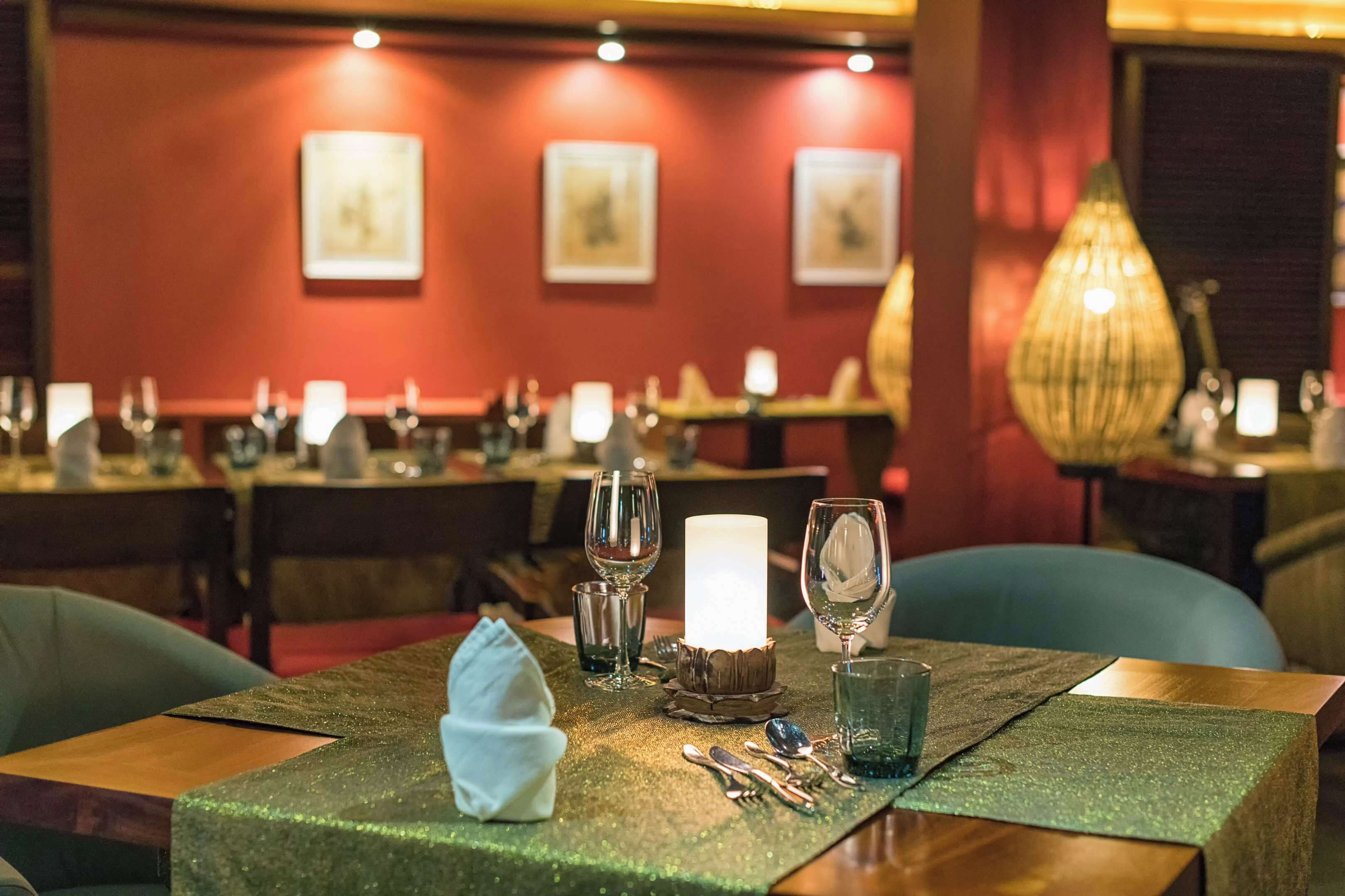 Een restaurantinterieur met gedekte tafels, met een groene tafelkleed, kaarsen en glazen.