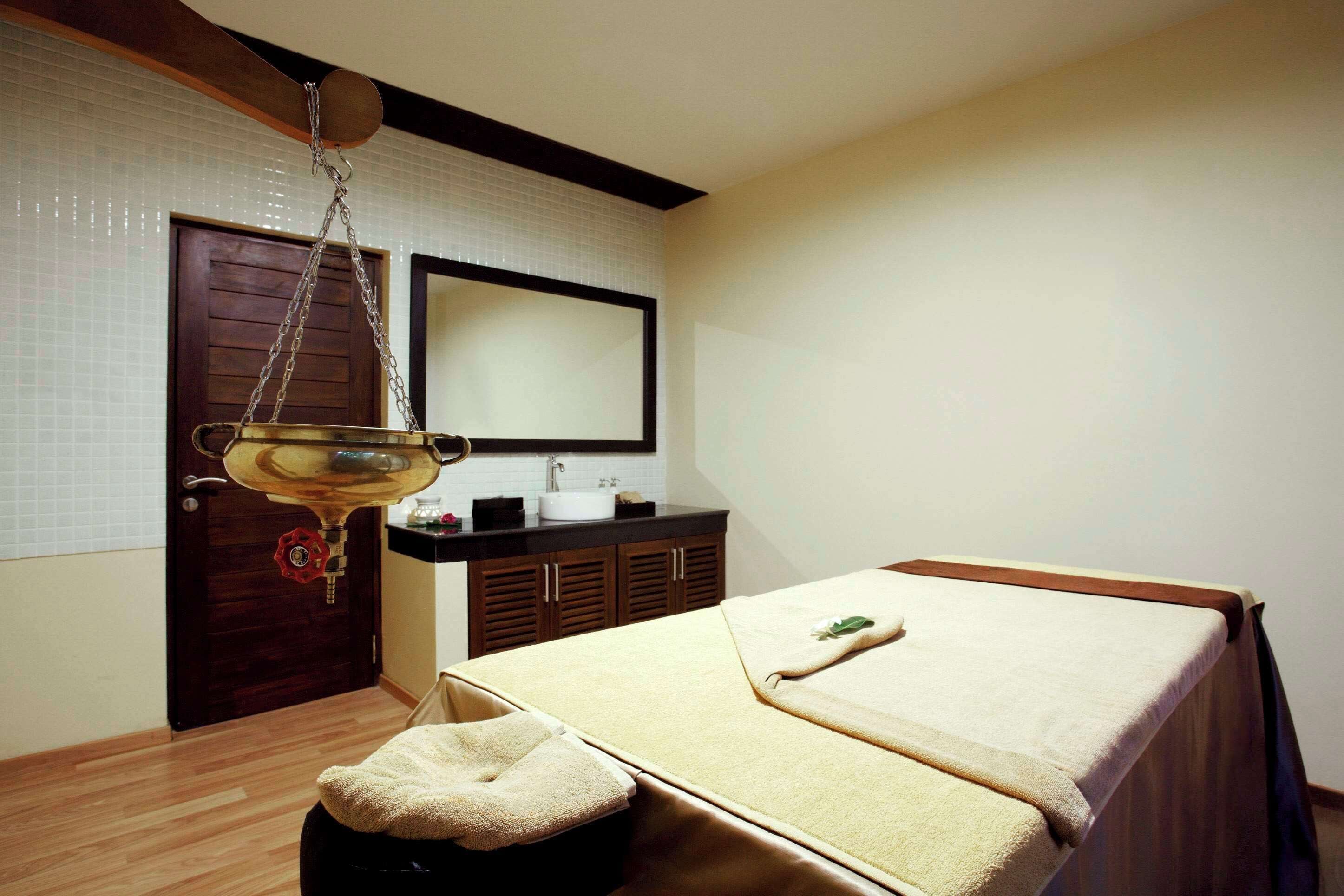 A room with a bed, a small stool, a sink, and a mirror.