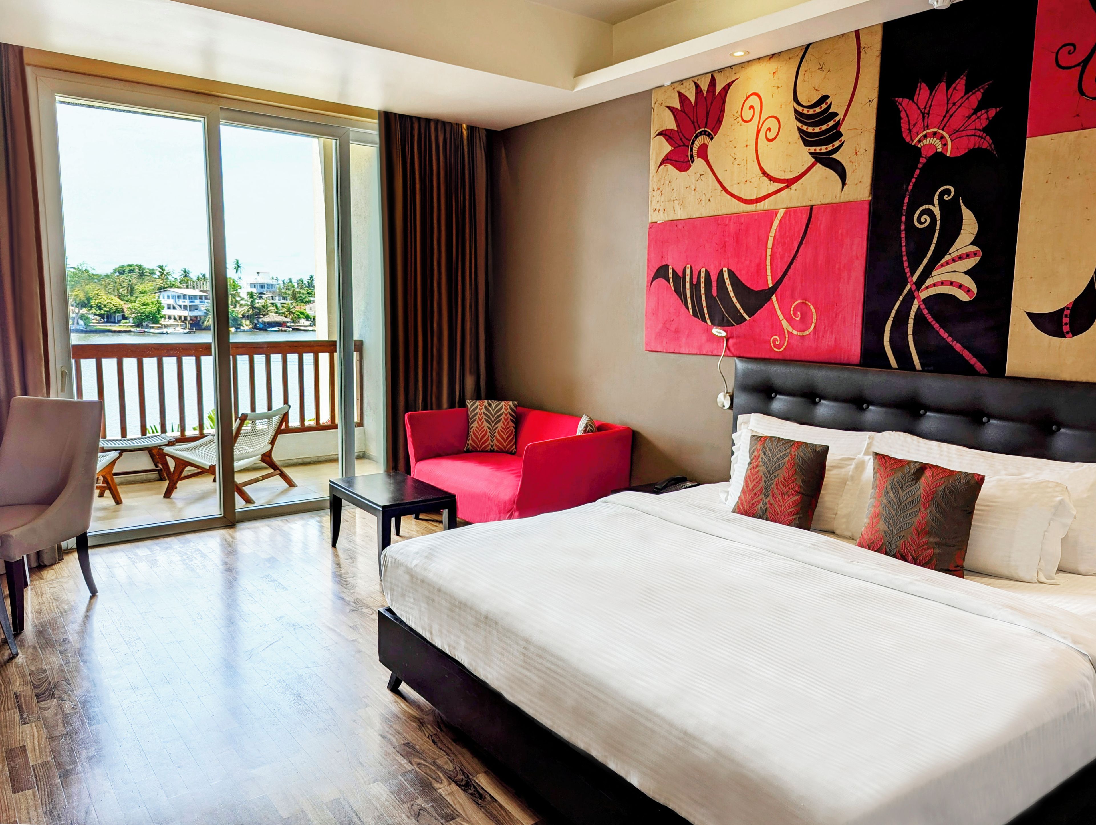 A hotel room with a bed, a red sofa, a small table, and a balcony with a view.