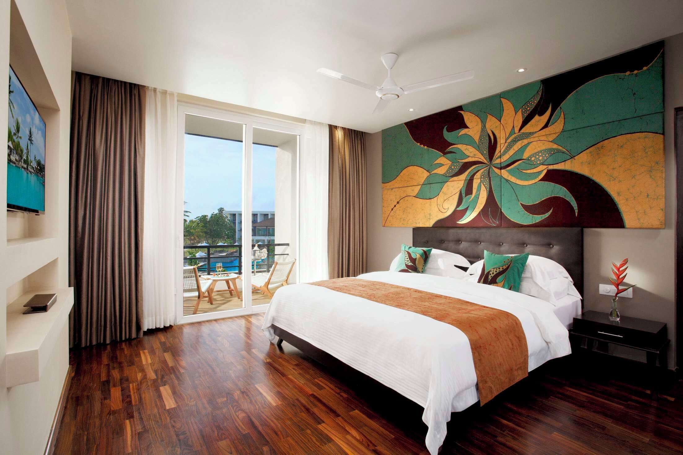 A spacious bedroom with a large bed, a ceiling fan, a view of the outdoors, and a painting on the wall.