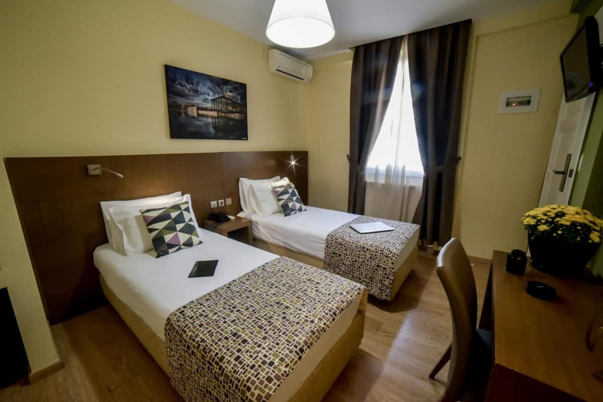 Une chambre d’hôtel avec deux lits, un bureau, une chaise, une télévision et un tableau au mur.