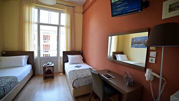 A hotel room with two beds, a desk, a chair, a lamp, a mirror, and a window with curtains.