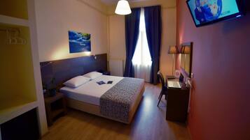 Habitación de hotel con cama, escritorio, televisor y ventana con cortinas.
