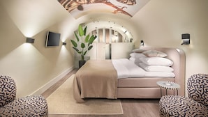 A modern bedroom with a curved ceiling, a bed with a beige blanket, patterned chairs, a small side table, and a potted plant.