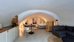 A compact, modern loft bedroom with a curved ceiling, a small dining area, a sofa, and a wooden cabinet.
