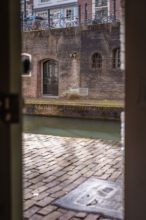 A view through a door of a brick building with a waterway in front, a brick pavement, and bicycles parked on the upper level.
