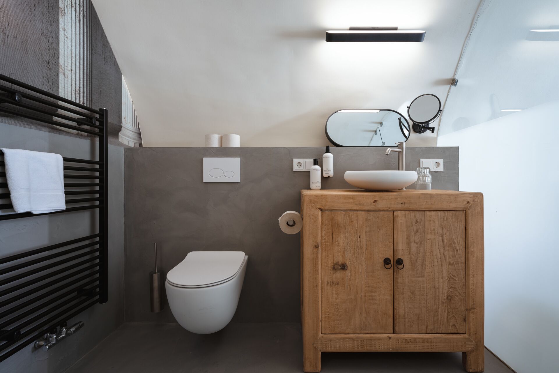 A modern bathroom with a wooden vanity, a white toilet, and a towel rack with a white towel.