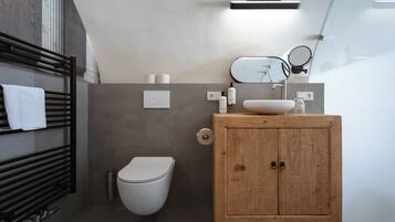 A modern bathroom with a wooden vanity, a white toilet, and a towel rack with a white towel.