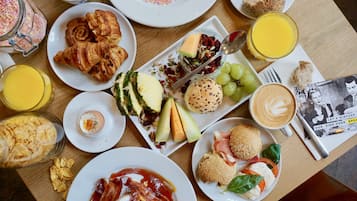 A breakfast table with croissants, eggs, cheese, fruits, and beverages.