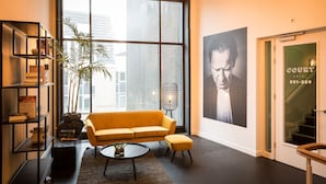 A modern hotel lobby with a large window, a yellow sofa, a bookshelf, and a poster on the wall.