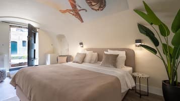 A bedroom with a large bed, a potted plant, and a mural on the ceiling.