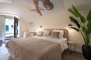 A bedroom with a large bed, a potted plant, and a mural on the ceiling.