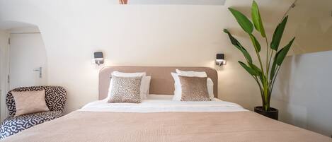 Habitación de hotel con una cama grande, dos lámparas fijadas a la pared, una planta en maceta y una obra de arte en el techo.