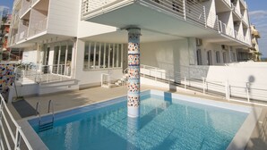 Un hôtel moderne doté d’une piscine, d’une façade blanche, de balcons et d’un design unique pour ses colonnes.