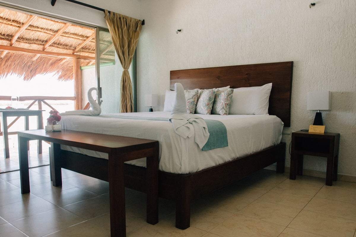 Una habitación de hotel con una cama, una mesita de noche de madera, una pequeña mesa y una silla.