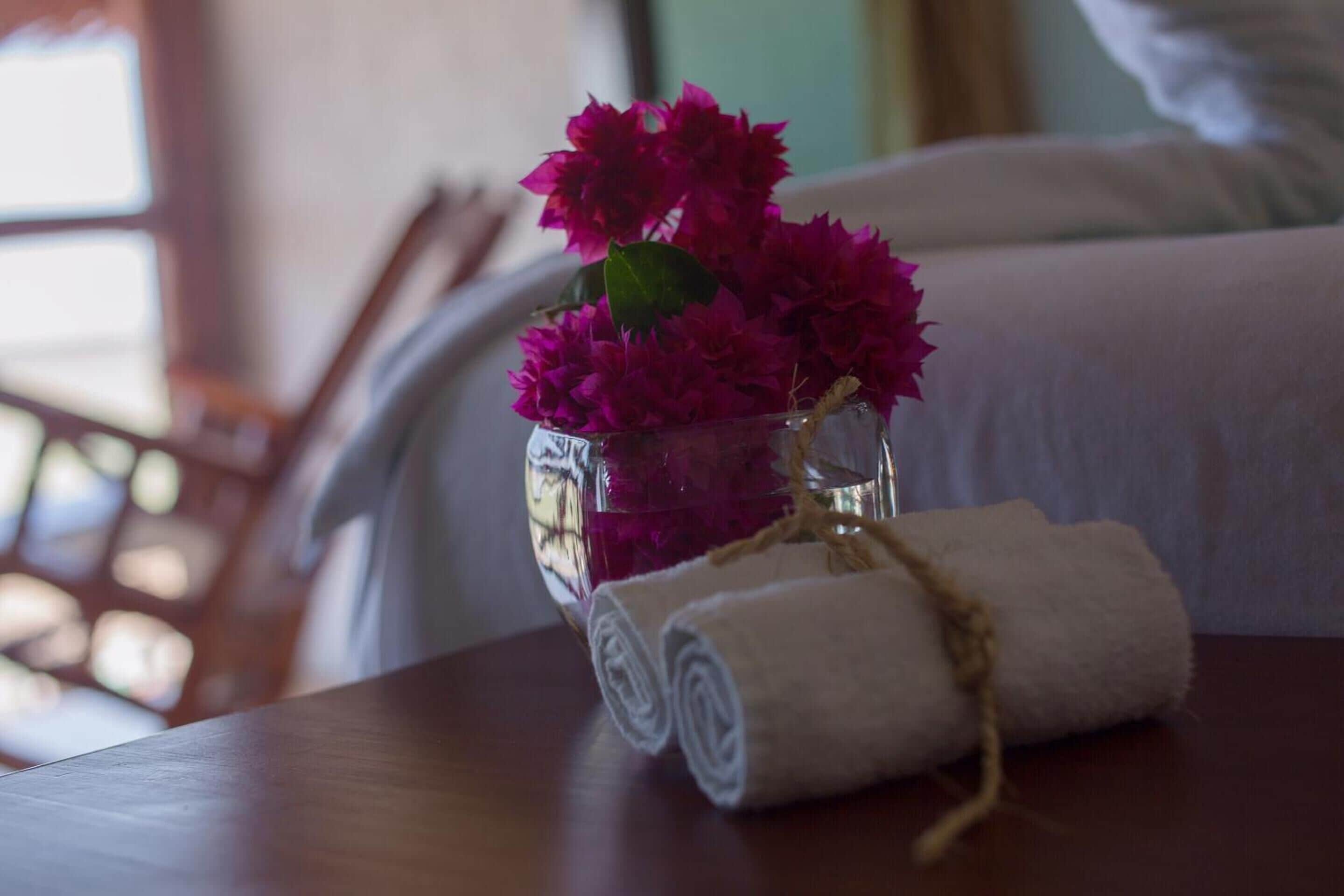 Une table en bois sur laquelle se trouve un vase en verre contenant des fleurs roses et une serviette blanche roulée, maintenue par une ficelle.