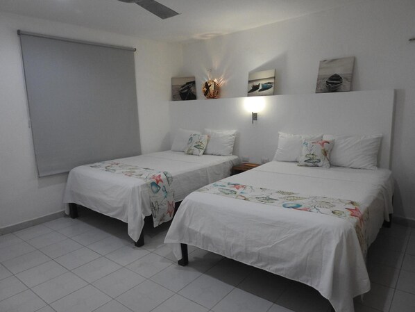 A room with two single beds, a ceiling fan, and artwork on the walls. - Hotel Villa de Pescadores (Río Lagartos)