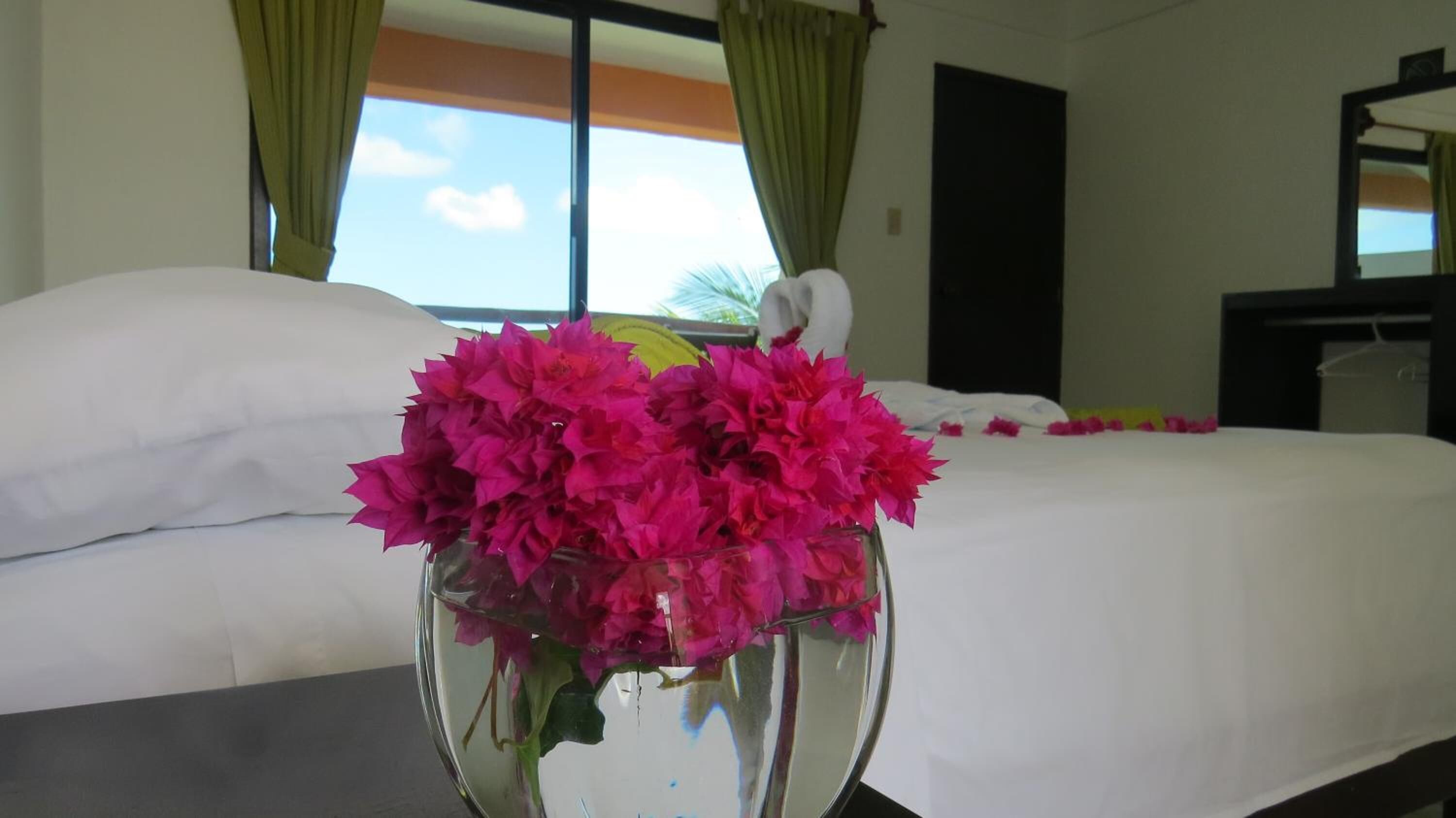 Una habitación de hotel con una cama, un jarrón de flores rosas y una ventana con cortinas.