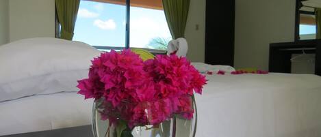 Una habitación de hotel con una cama, un jarrón de flores rosas y una ventana con cortinas.