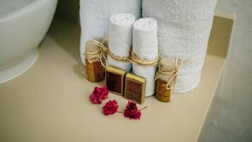 Une salle de bain avec une baignoire blanche, une serviette blanche et trois petits flacons de produits de bain.
