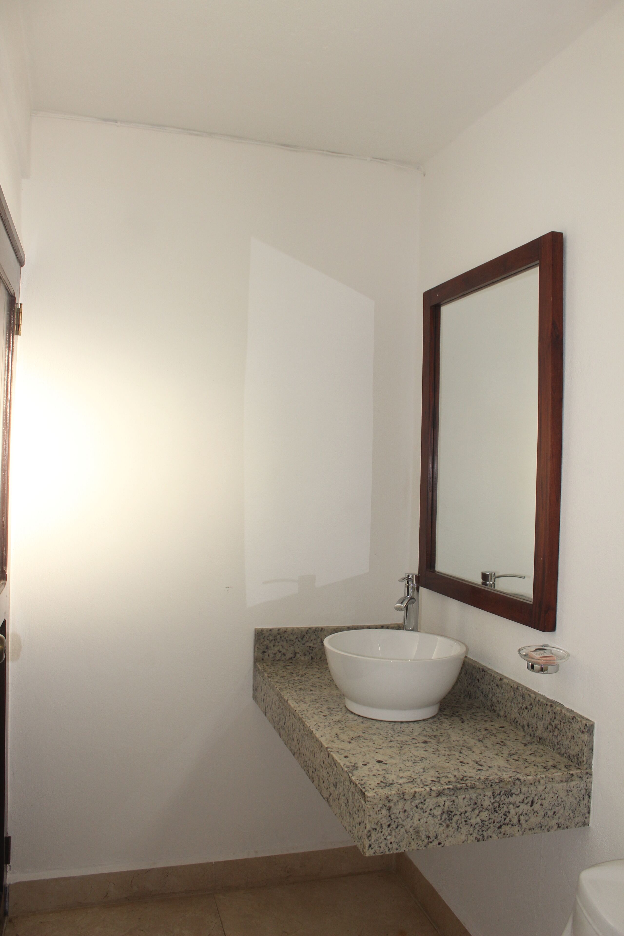 Un baño con lavamanos blanco, encimera de granito y espejo con marco de madera.