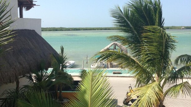 Vista de una playa con una estructura de techo de paja, palmeras y un mar azul cristalino.