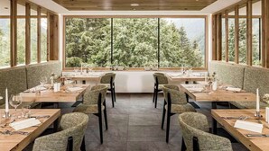 A dining area with wooden tables and chairs, large windows with a view of trees. - Falkensteiner Hotel Antholz (Rasun Anterselva)