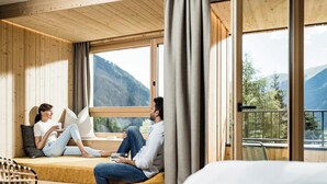 A cozy room with wooden walls and large windows, a sofa, and a chair. - Falkensteiner Hotel Antholz (Rasun Anterselva)