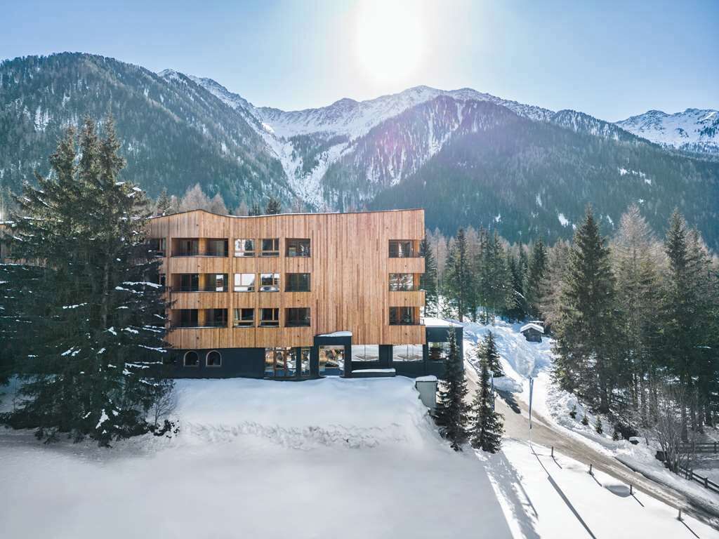 Un bâtiment moderne en bois, à plusieurs étages, entouré de montagnes enneigées et de pins.