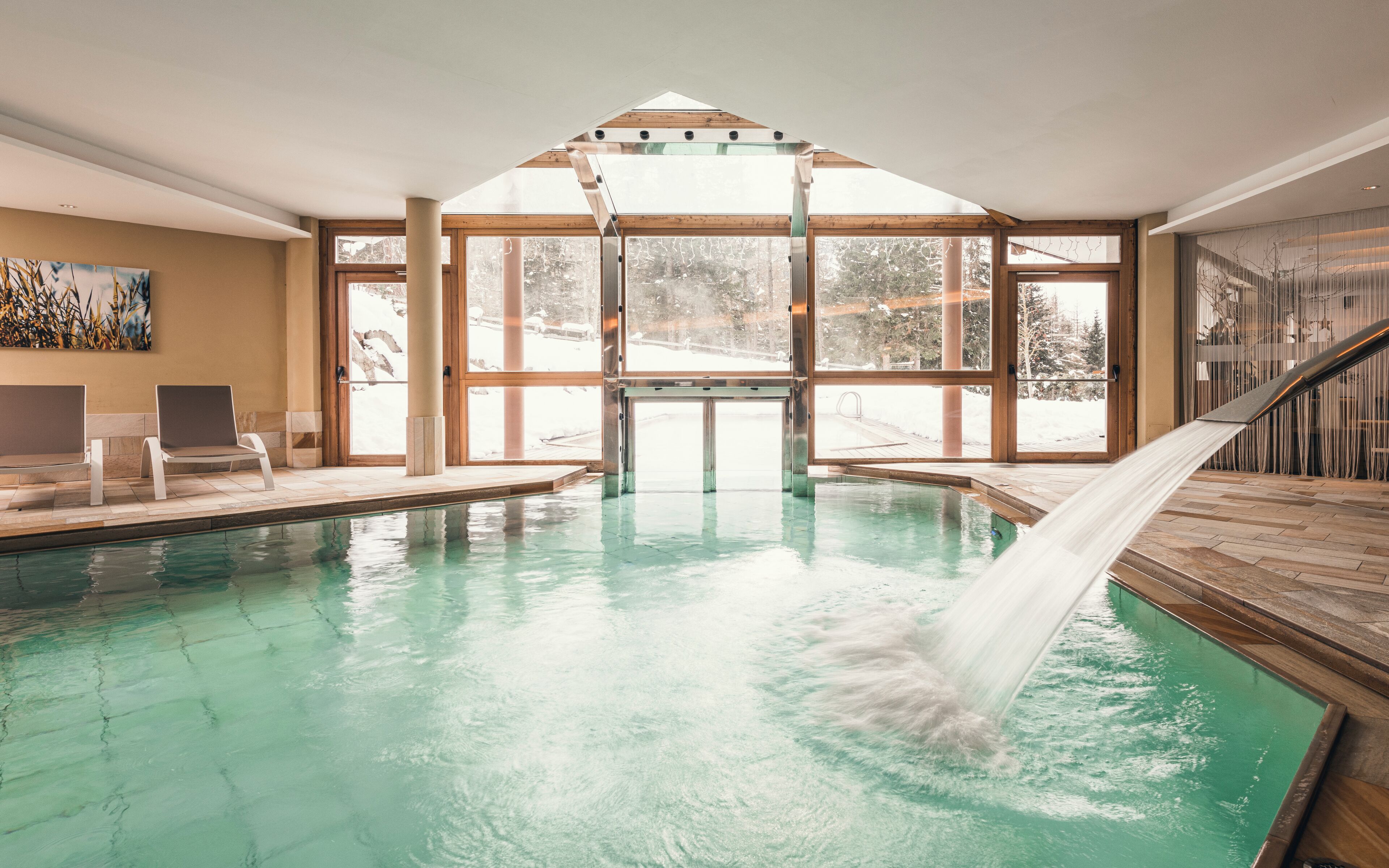 Une piscine intérieure avec des parois en verre transparent, une cascade et une vue sur un paysage enneigé.