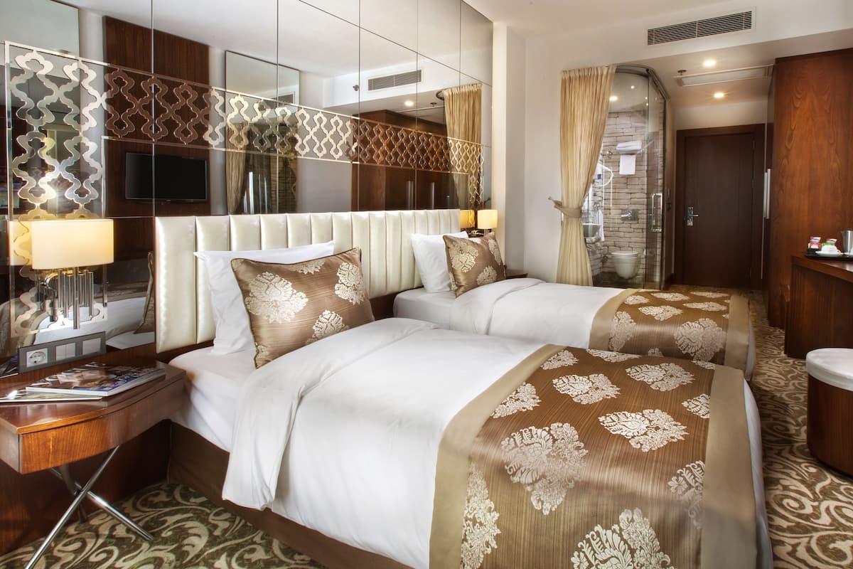 A hotel room with two beds, a large mirror, a TV, and a bathroom with a shower and toilet.