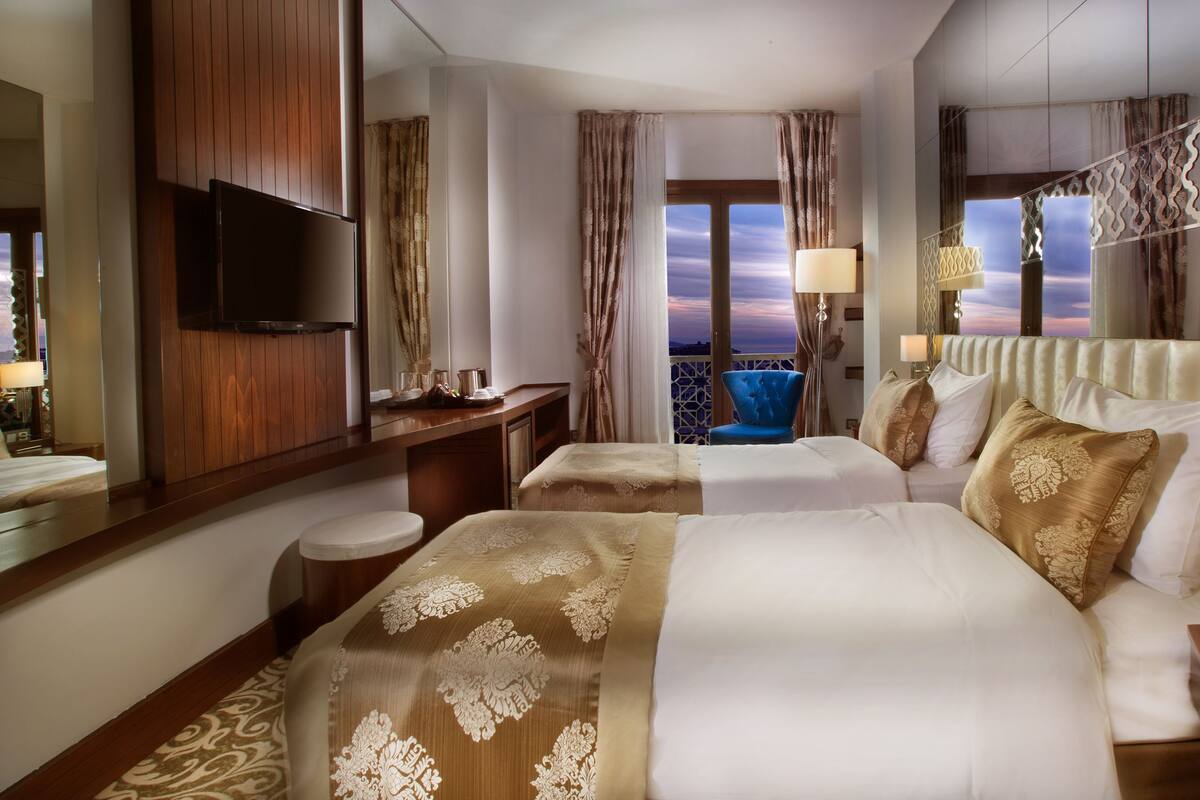 A hotel room with two beds, a TV, a balcony with a view, and a decorative railing.