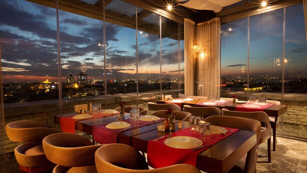 A restaurant with a city view at dusk, featuring a table set for dining with chairs and a large window overlooking the cityscape. - Pera Center Hotel (Istanbul)