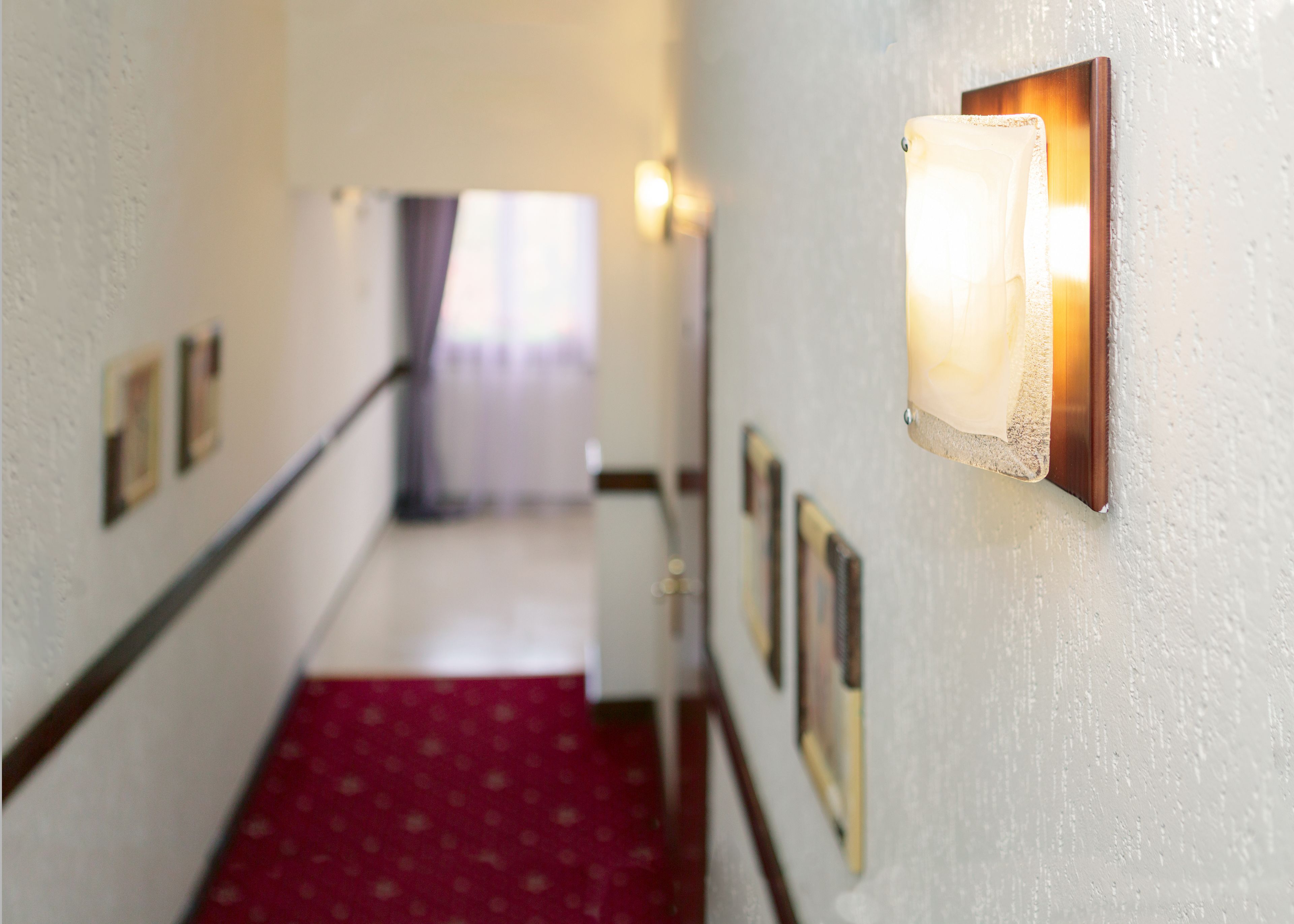A hallway with a red carpet, framed pictures on the walls, and a light fixture on the right.