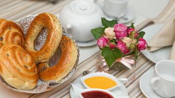 Una mesa con bagels, una tetera, un ramo de flores y dos recipientes pequeños de mermelada.