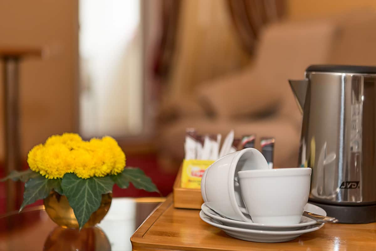 A table with a coffee pot, a vase with yellow flowers, and stacked white cups and saucers.