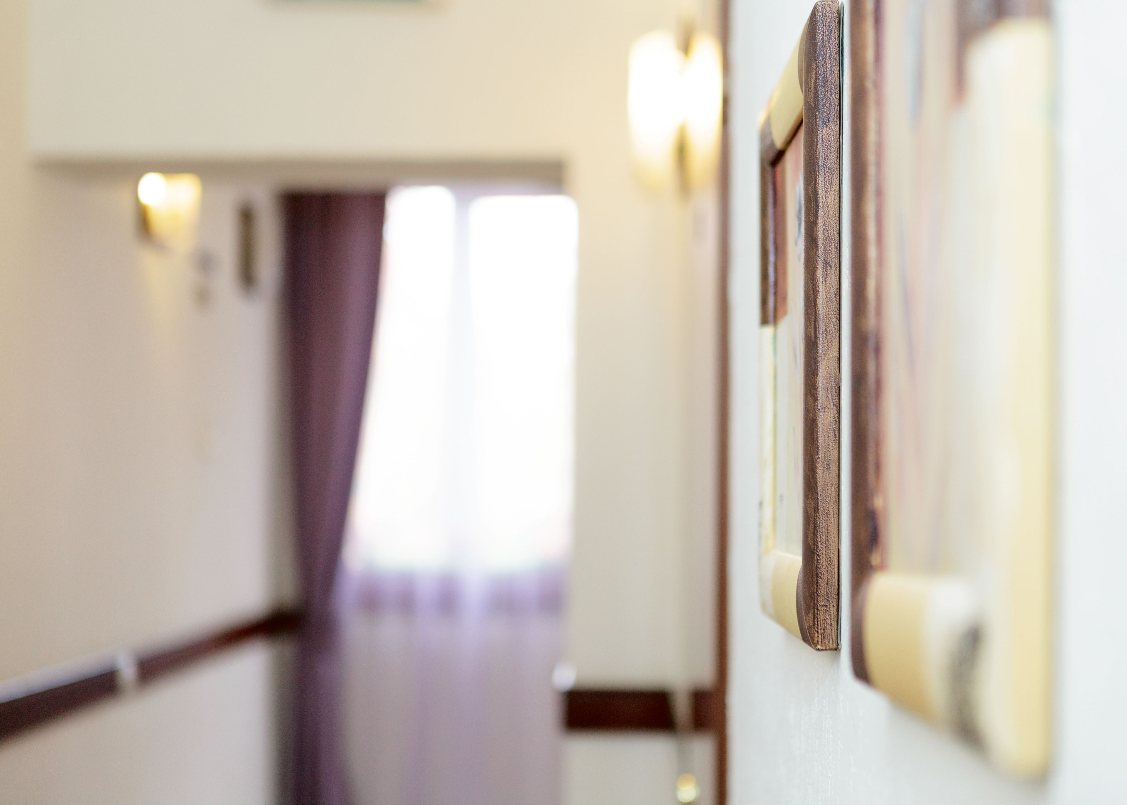 Un couloir d’hôtel avec un plancher en bois, une porte dotée d’un interrupteur et un luminaire fixé au mur.