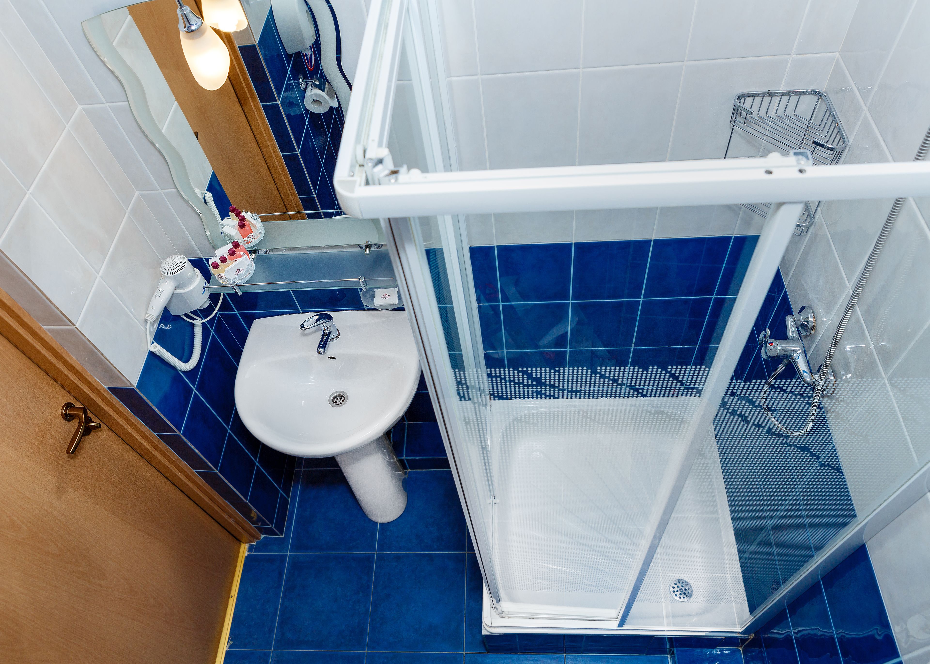 Un baño con un lavamanos blanco, azulejos azules, una cabina de ducha de vidrio y una puerta de madera.