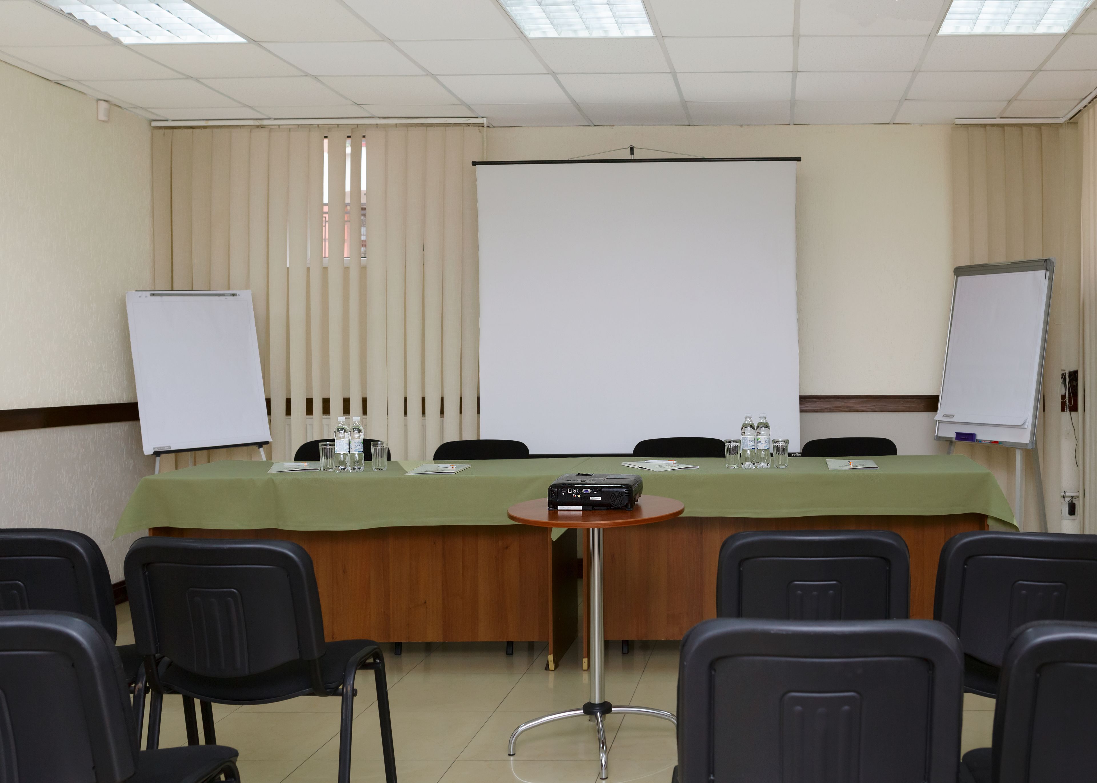 Un salón de conferencias con una larga mesa, sillas, un proyector y dos pizarras blancas.