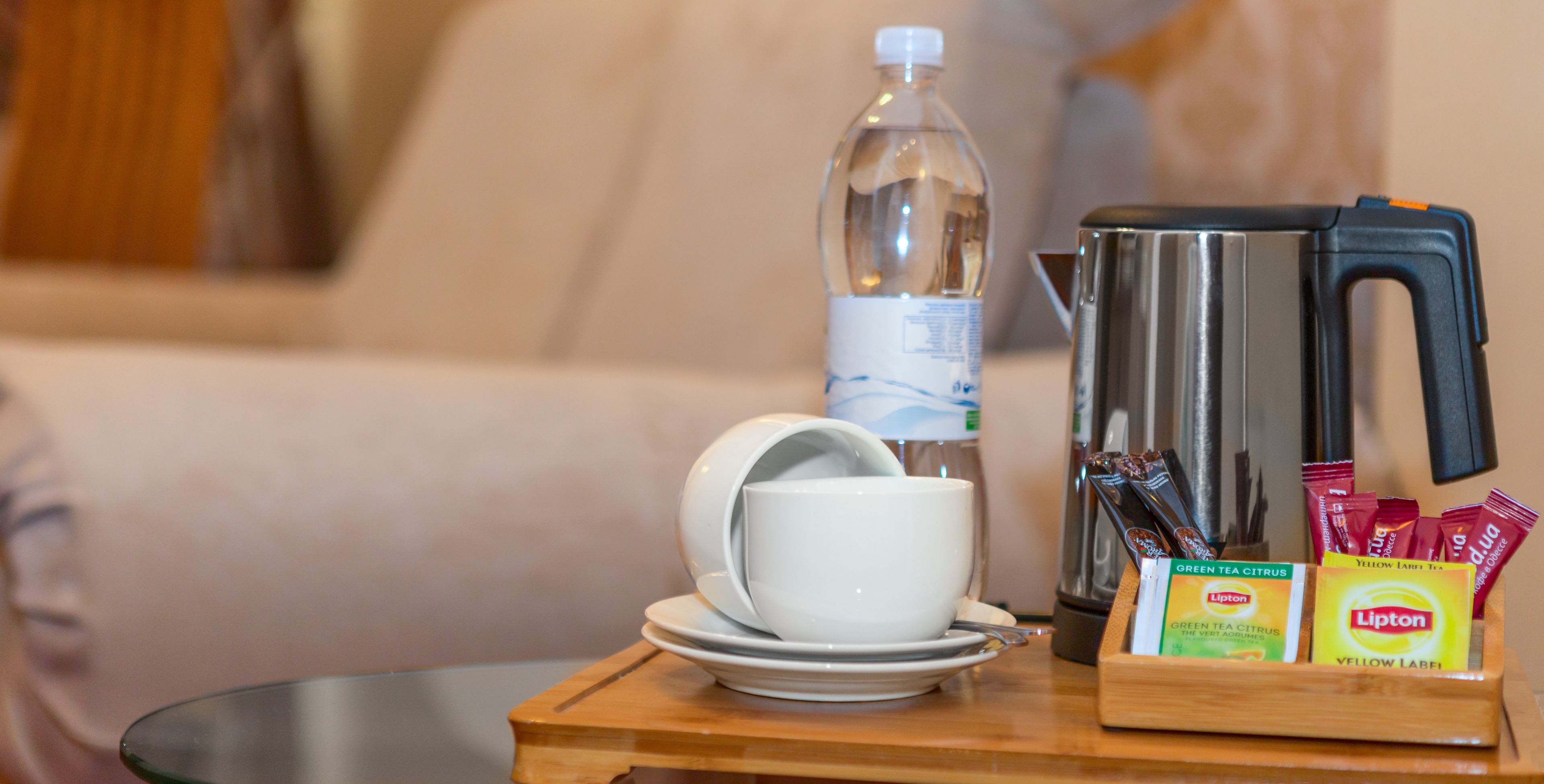 Une petite table sur laquelle se trouvent une tasse et une soucoupe blanches, une bouteille d’eau, une bouilloire et des sachets de thé Lipton.