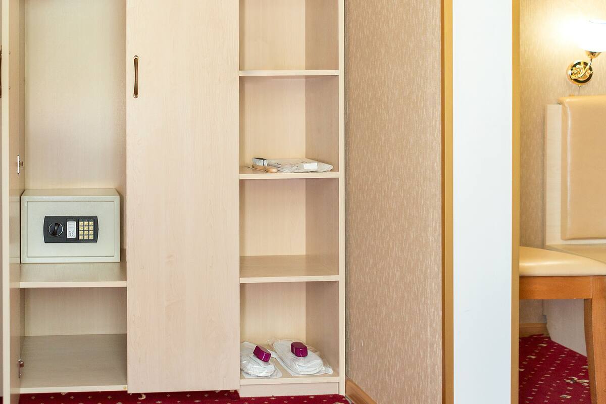A hotel room with a wardrobe, a bedside table with a lamp, a small cabinet, and a bed.