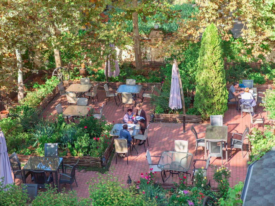 Un patio al aire libre con mesas y sillas, rodeado de follaje y plantas.