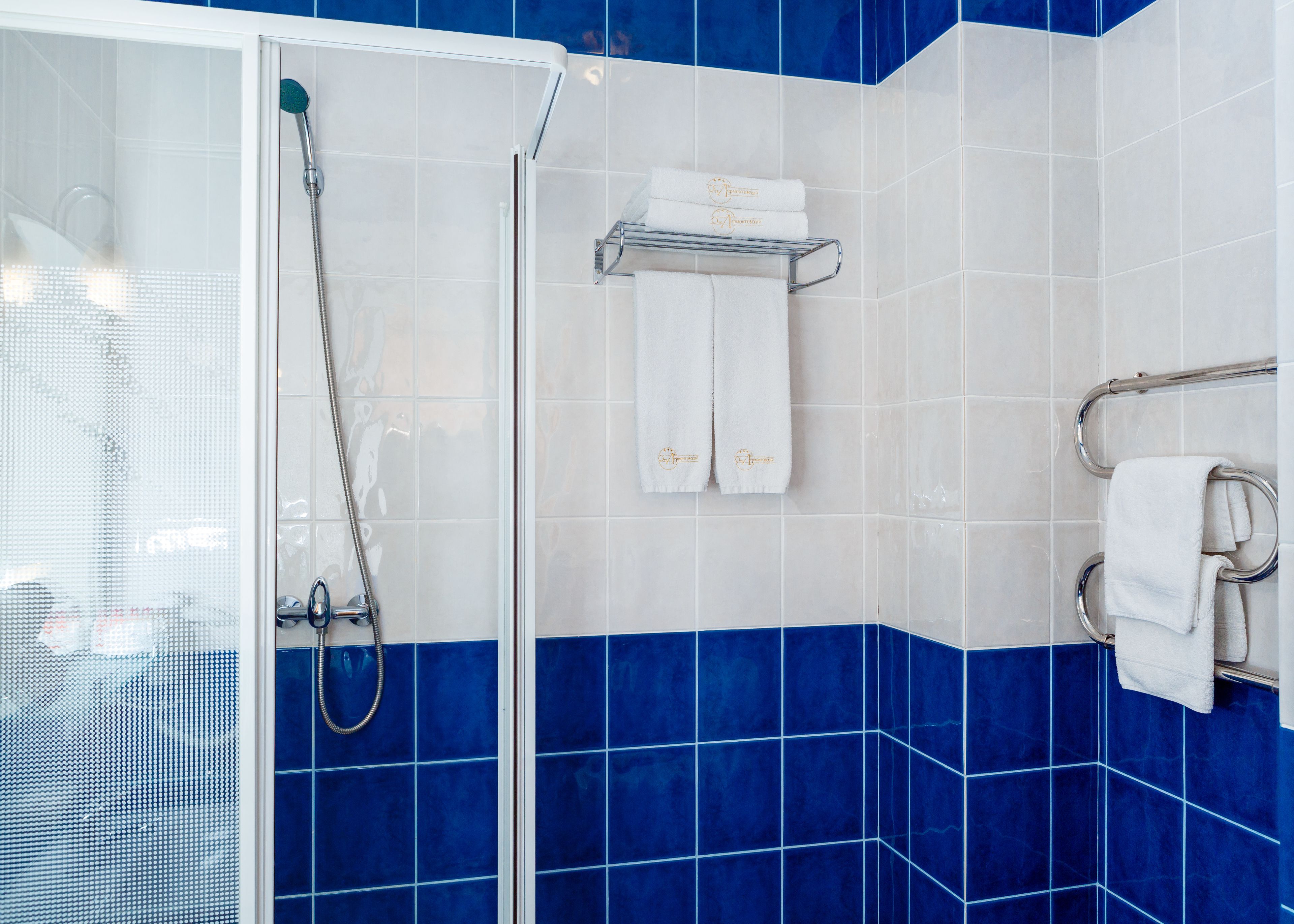 A bathroom with a glass shower enclosure, a towel rack with folded towels, and blue-tiled walls.