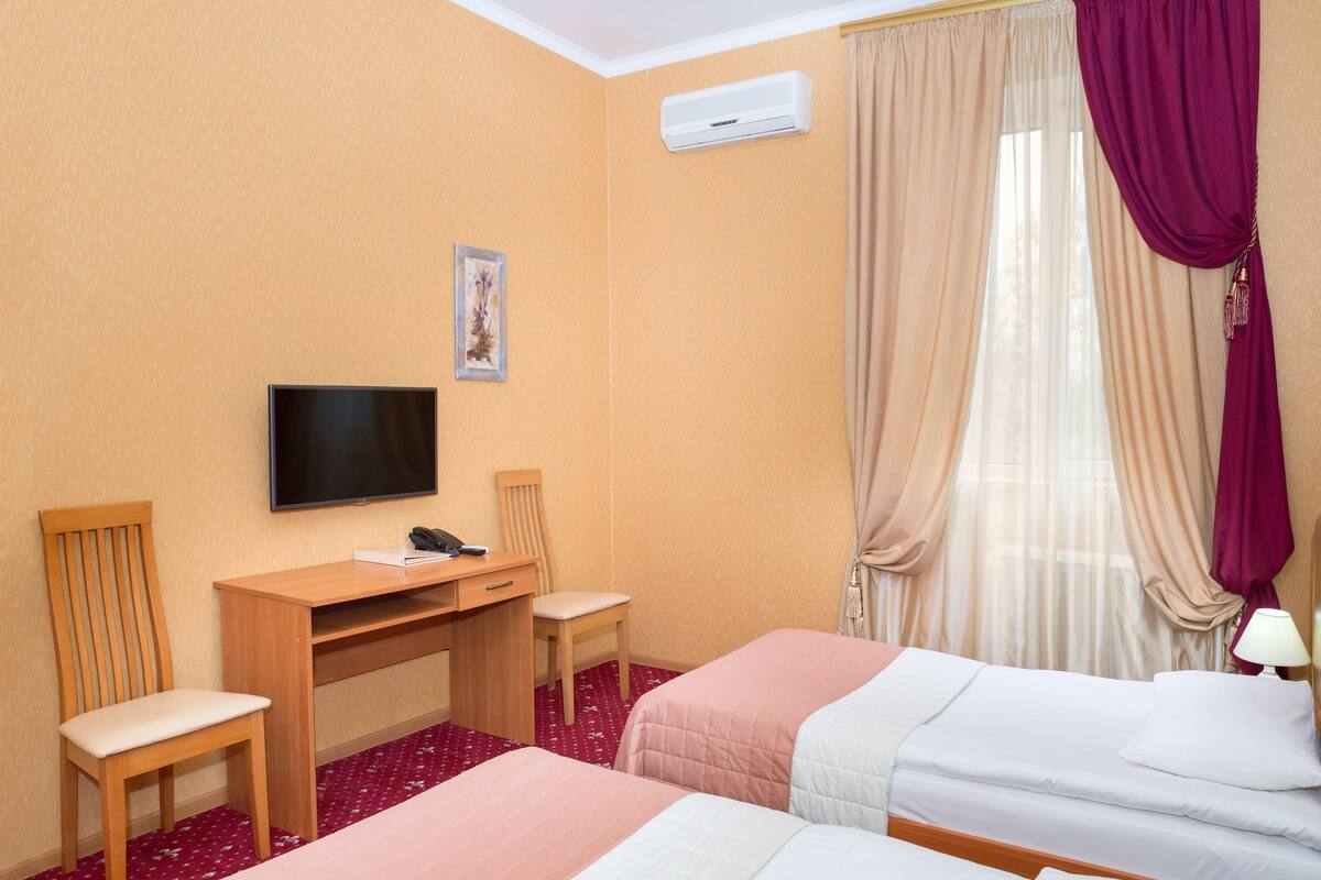 A hotel room with two beds, a desk with a chair, a television, and an air conditioning unit.