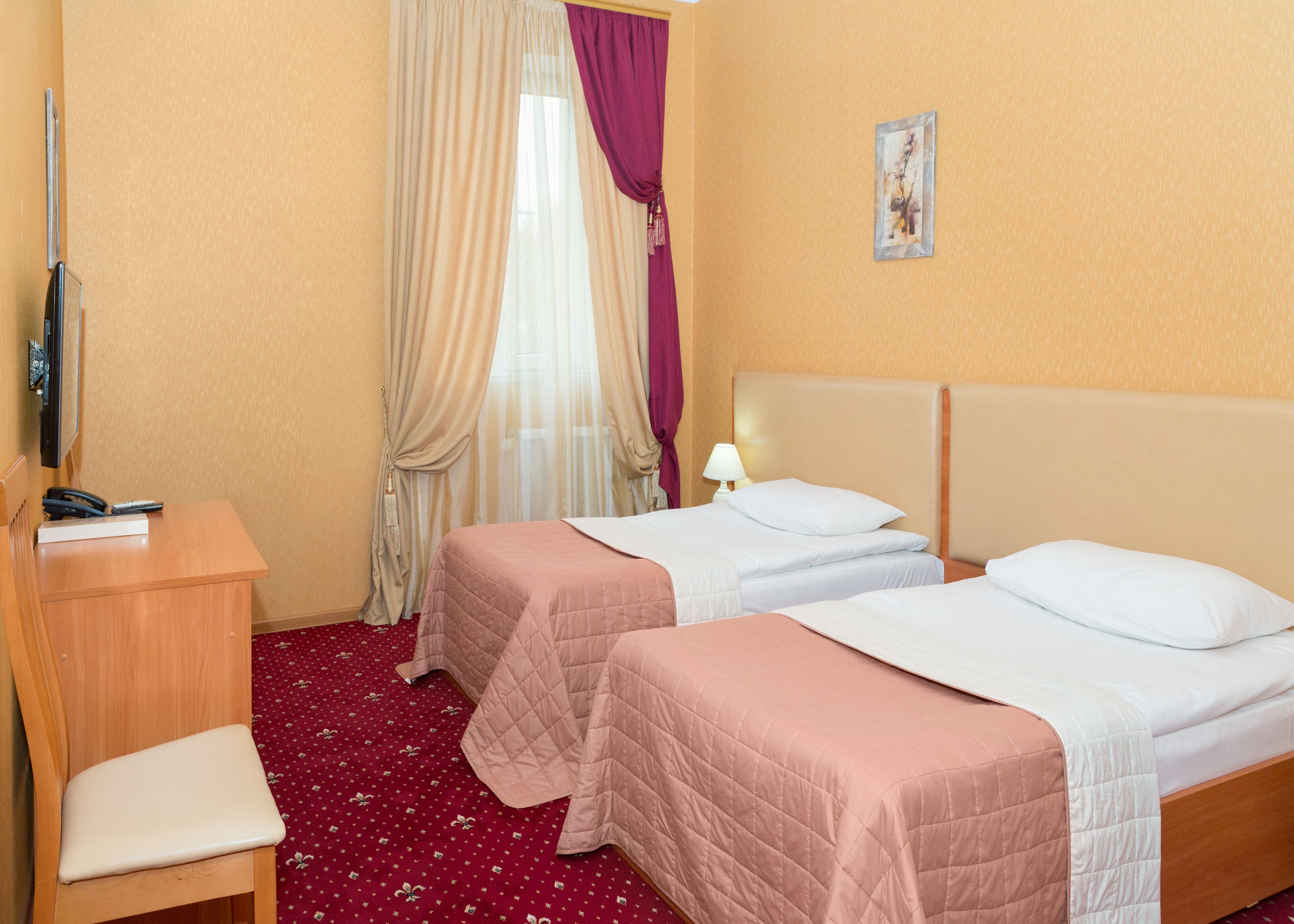 Camera d'albergo con due letti, una scrivania, una sedia, una televisione e una finestra con tende.