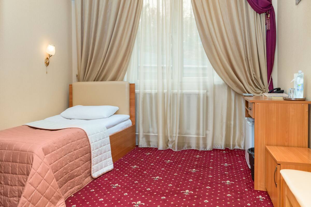 A small, neatly arranged bedroom with a single bed, a bedside table, a desk, and a chair.