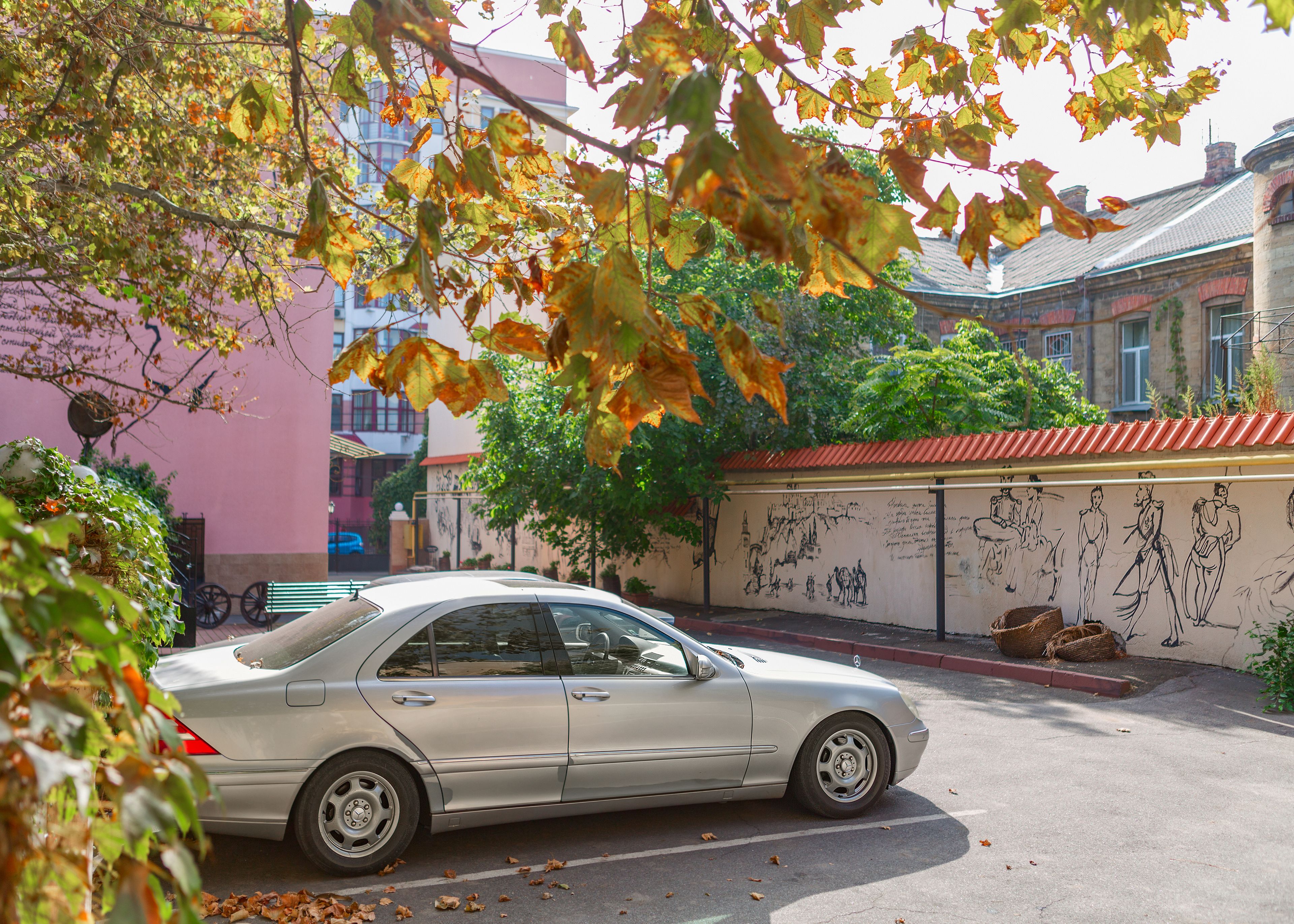 Une voiture argentée est garée devant un immeuble dont la façade est ornée d’une fresque.