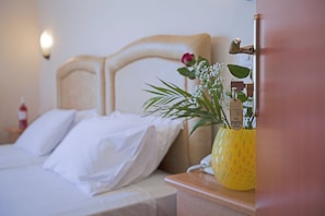 A hotel room with a bed, a nightstand with a telephone, and a vase with flowers. - Hotel Epidavria (Nafplio)